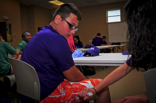 Person using an EpiPen on another person's leg in a training session.