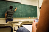 Student texting while teacher writes on board.