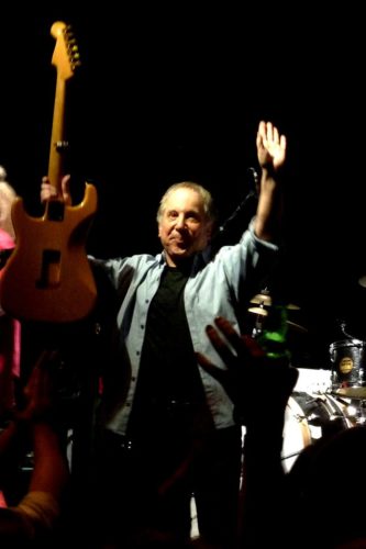 Paul Simon raising guitar in concert in 2011.