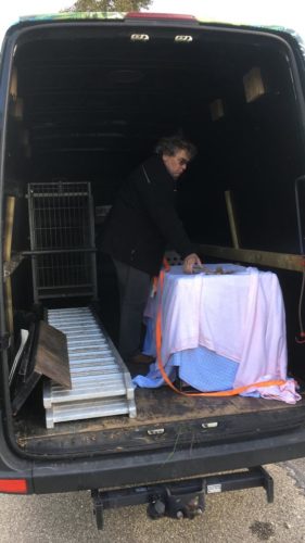 Man standing in back of an open van next to a covered cage.