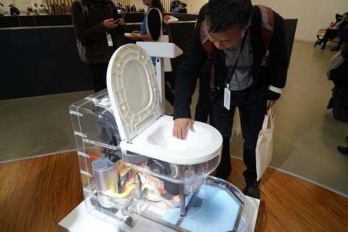 A man inspects a new processing toilet with a clear base.