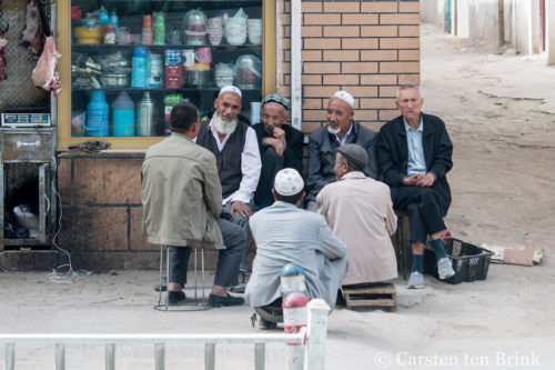 Uighur men sit on sidewalk in Yarkand and hold a discussion