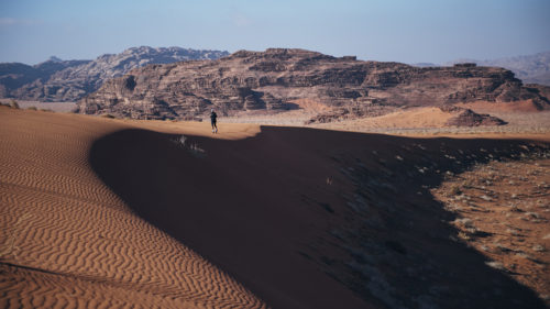 Ms. Guli running across desert dunes, with mountains in the background.