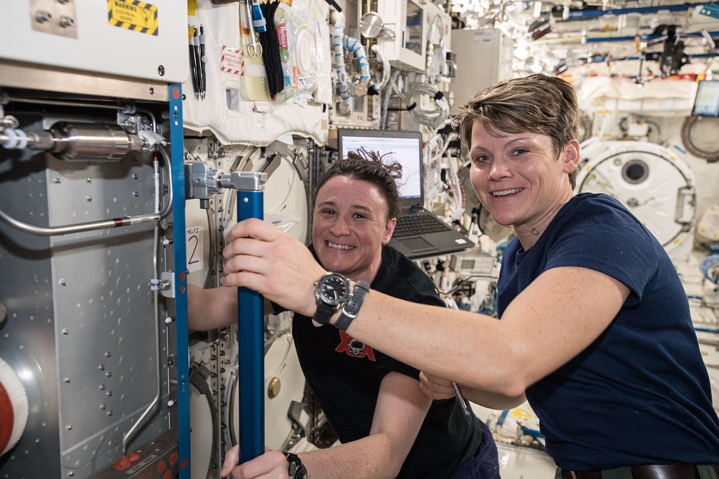 NASA astronauts Serena Auñón-Chancellor (background) and Anne McClain work inside the Japanese Kibo laboratory module cleaning vents to maintain air circulation aboard the International Space Station.