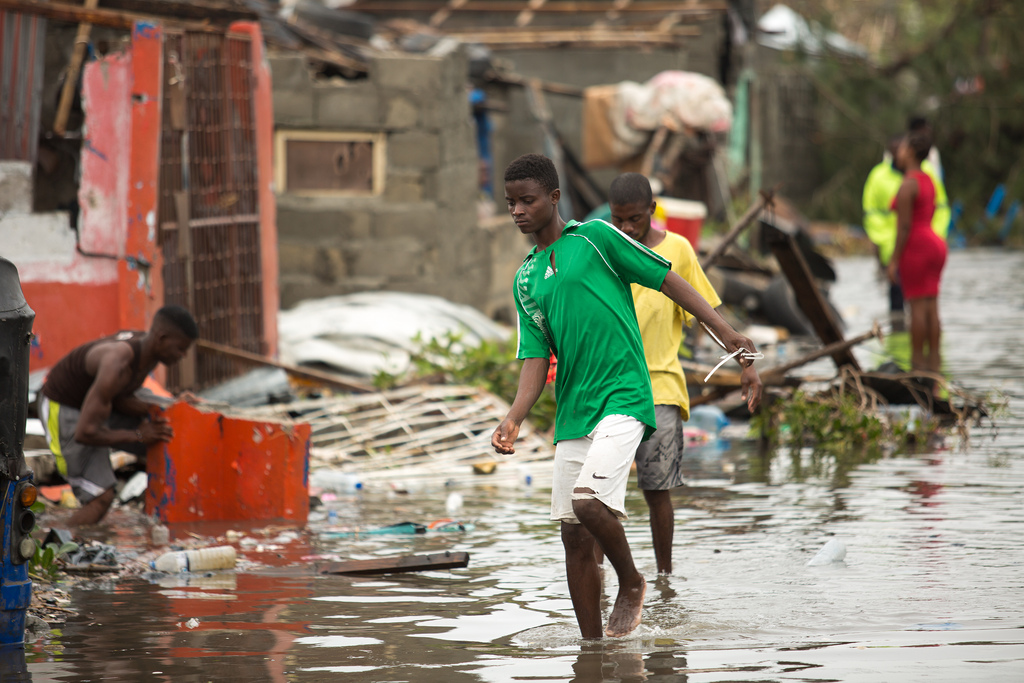 Boys wading through water as people try to rebuild their homes.