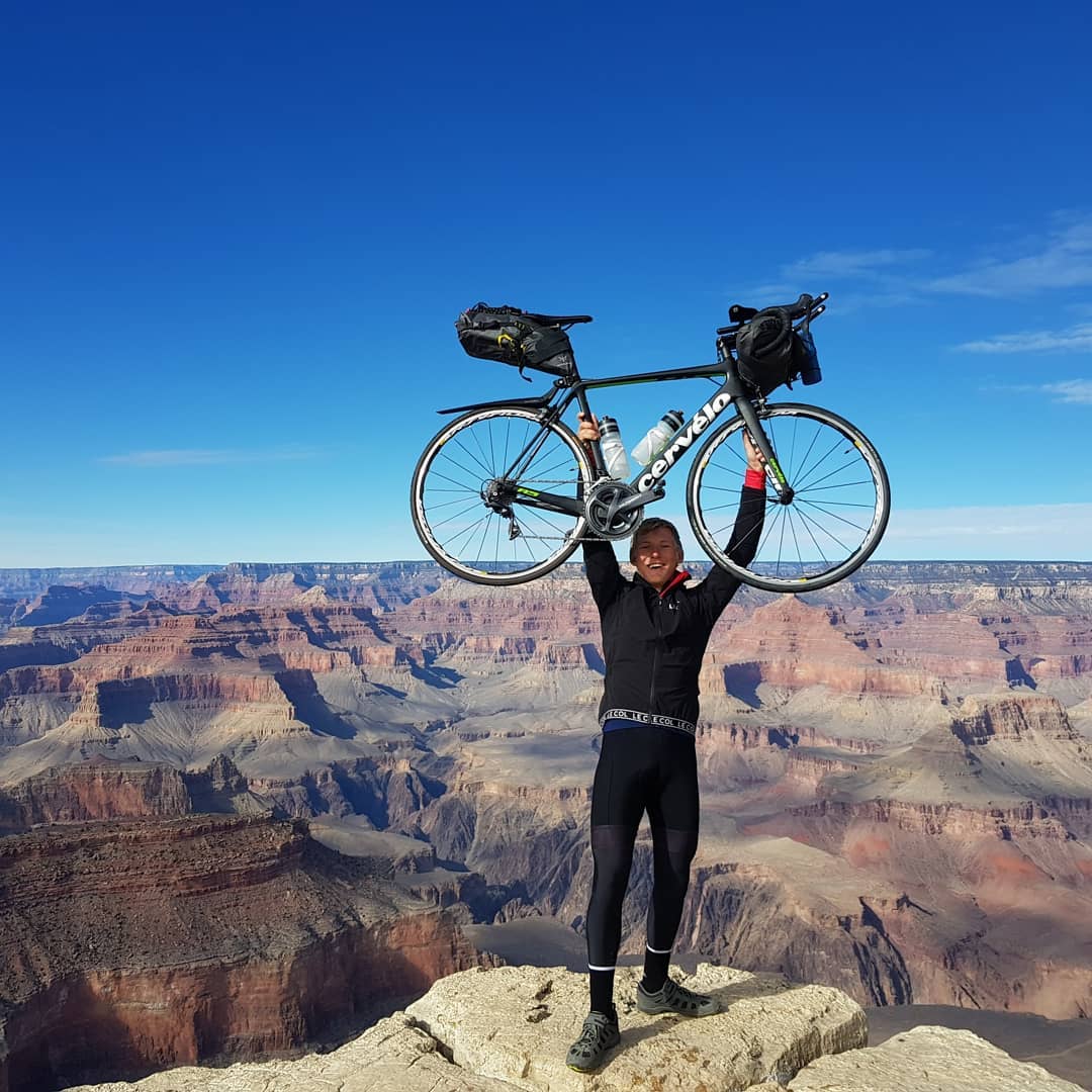 Charlie raises bike overhead with Grand Canyon backdrop.