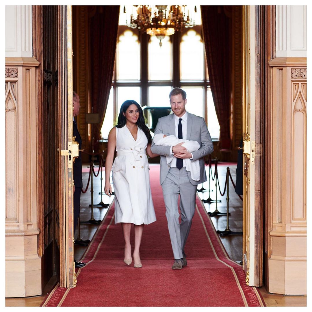 The Duke and Duchess of Sussex walking through a doorway with their baby.