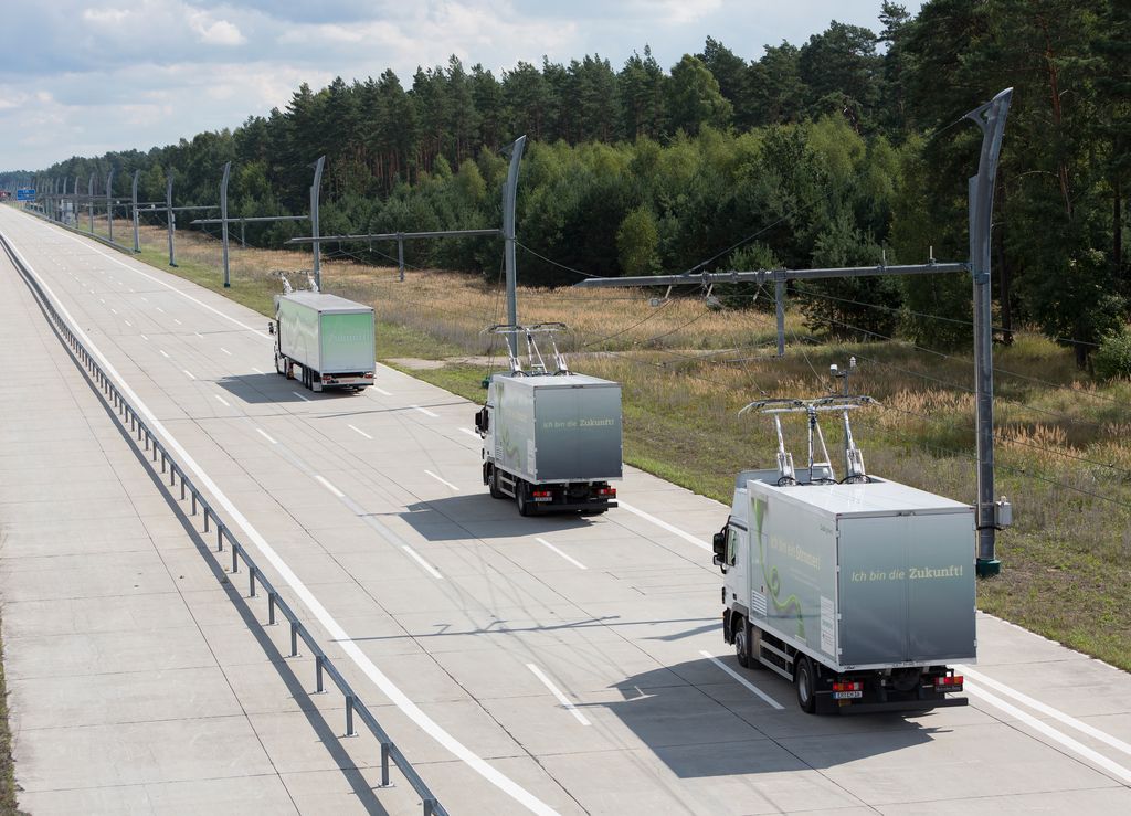 Three hybrid trucks travel on an eHighway, charging from an overhead cable system.