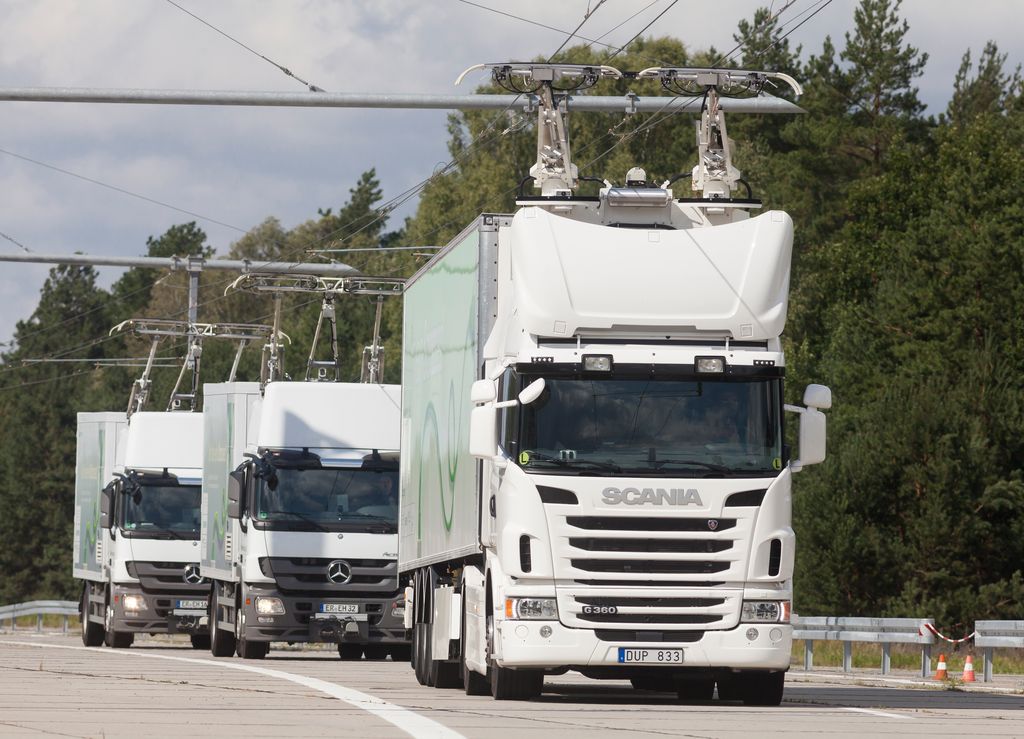 Three hybrid trucks travel on an eHighway, charging from an overhead cable system.