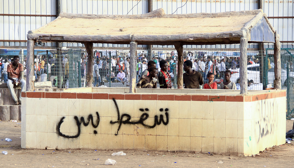 Sudan Revolution - Tasgut Bas spray painted on a wall, crowd behind