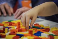 A child's hand reaches for a Braille Lego brick.