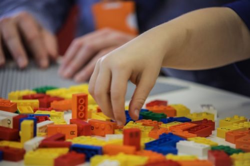 A child's hand reaches for a Braille Lego brick.