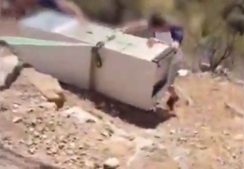 A man works to get a refrigerator back up a hill.