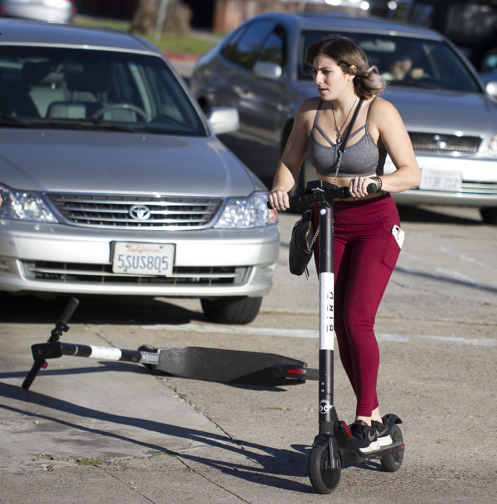 Woman on scooter in traffic, dropped scooter in background