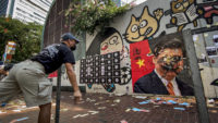Hong Kong protester throws something at a defaced painting of Chinese President Xi Jinping.