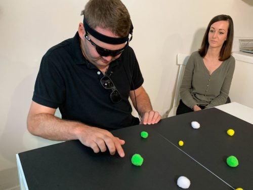 Jason Esterhuizen, who lost his vision in a car accident, practices finding objects with his wife, Sumarie. A video camera on his glasses signals an experimental device in his brain, enabling him to distinguish light from dark.