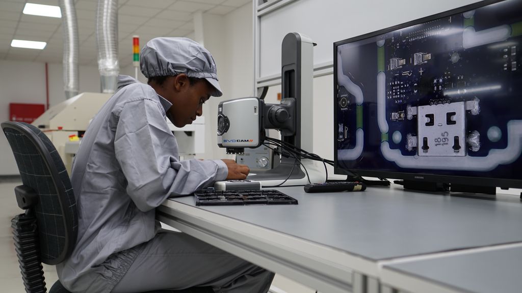 Technician examines phone circuitboard with magnifying camera.