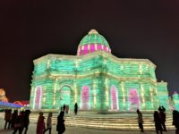 Large, domed building made of ice, lit with green and pink light, at the Harbin Ice and Snow Sculpture Festival, 2018