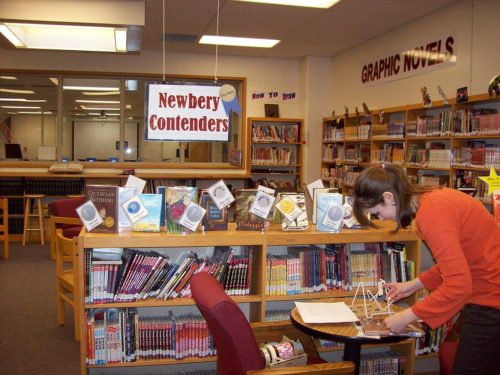 Librarian shelving under a sign saying Newbery Medal Contenders.