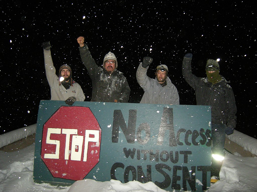Unist'ot'en Camp members holding a large sign reading "No access without consent"