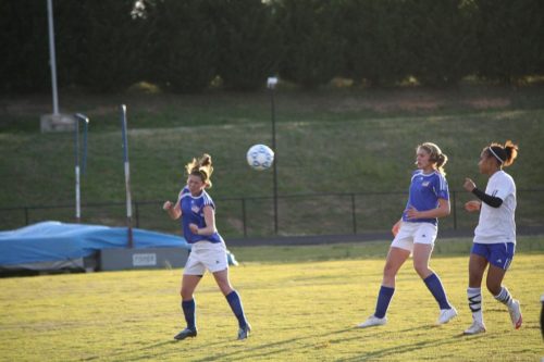 Girl heads soccer ball toward other players.
