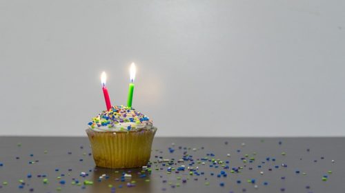 Picture of a cupcake with two lit candles on it.