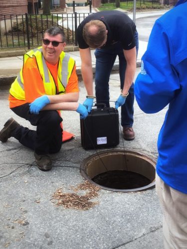 Biobot workers taking a field sample at an open manhole cover.