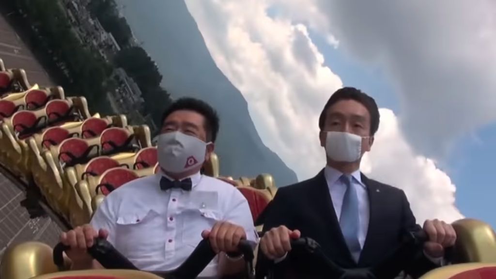Two men in business suits ride a Fuji-Q Highland rollercoaster with serious expressions.