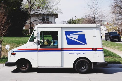 A mailman sitting in a mail truck sorting mail parked outside of a house in Tulsa