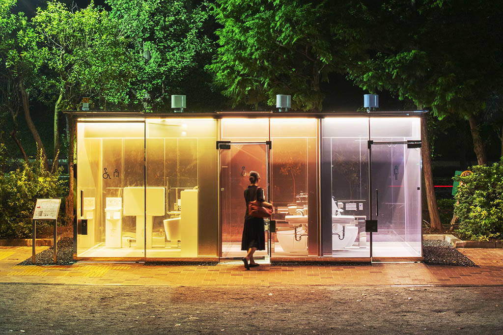 A woman enters transparent toilets designed by Shigeru Ban at night.