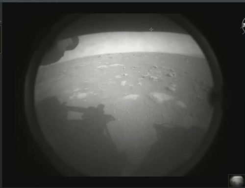 This is the first image NASA’s Perseverance rover sent back after touching down on Mars on Feb. 18, 2021. The view, from one of Perseverance’s Hazard Cameras, is partially obscured by a dust cover. A grey-scale image of a dusty, rocky Mars surface, with the shadow of the Perseverance Rover seen in the foreground.