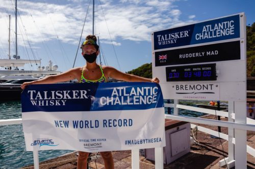 Jasmine Harrison stands in front of a board showing her time and holding a banner that says "New World Record".