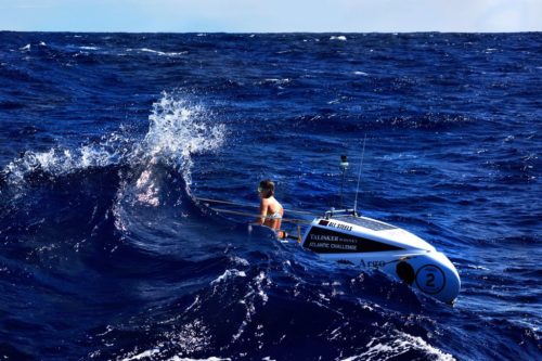 Jasmine Harrison in her boat with a large wave breaking over the boat.