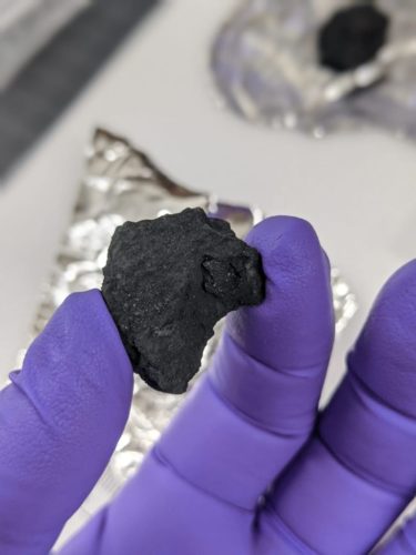 A carbonaceous chondrite meteorite found in the UK being held in a gloved hand.
