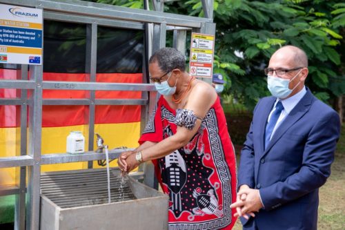 eSwatini's acting Prime Minister Themba Masuku washes his hands at a solar hot water station in Lobamba, eSwatini while Robert Frazer, head of Frazer Solar, looks on.