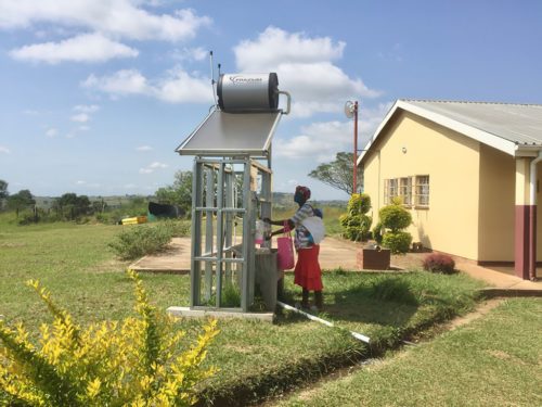 A woman with a baby washes her hands at a new solar hot water station at a health clinic in eSwatini.