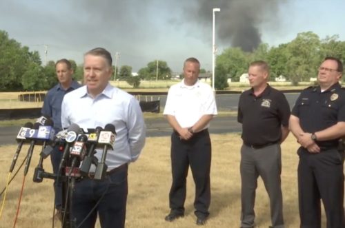 Bill Synder, VP of Operations for Lubrizol speaks to reporters about the Chemtool fire in Rockton, with smoke rising in the background.