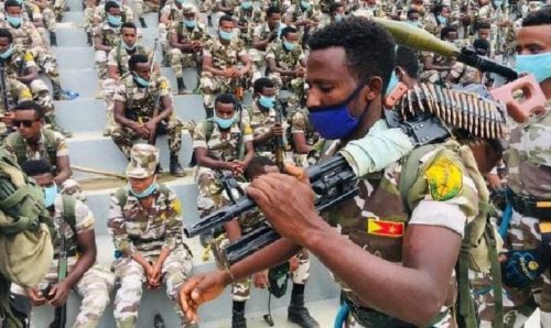 A man with a machine gun walks in front of seated soldiers belonging to the Tigray Defense Force,