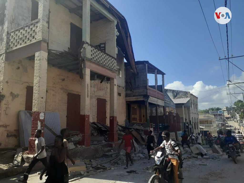 Haitians on motorcycles and on foot move down the street, looking at buildings damaged by the August 14 earthquake.