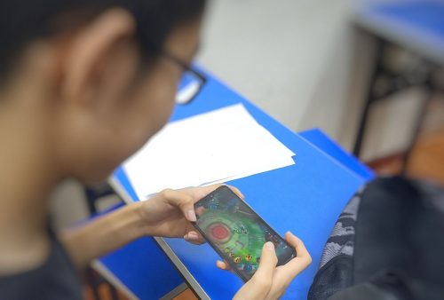 Student playing Wangzhe Rongyao video game on a smart phone.