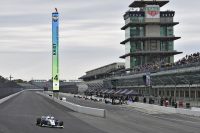 Indy Autonomous Challenge: A self-driving car drives along the track in front of the grandstand at the Indianapolis Motor Speedway.
