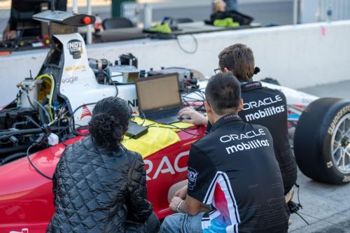 Indy Autonomous Challenge: Students work on the program for their self-driving car. Three students in front of a laptop set on the edge of a self-driving car and connected to it by wires.