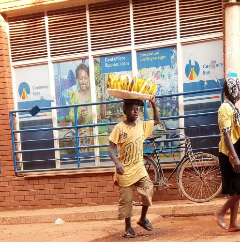 A young boy in Uganda carrying a large tray bananas on his head to sell.