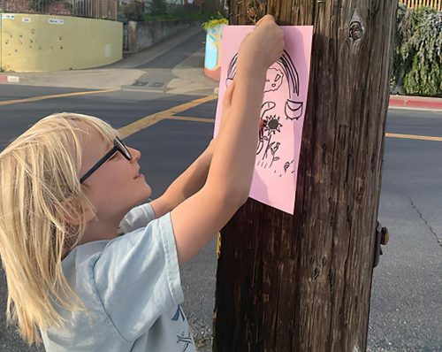 A child hangs a sign on a telephone pole.
