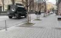 Solemn Kyiv copes with bombs and gunfire. Military vehicles roll down a city street.