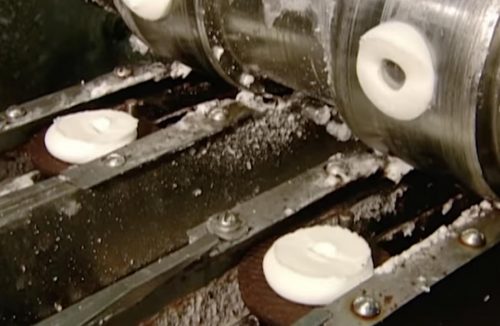 Image of cream squirted on one wafer of a sandwich cookie on a factory line.