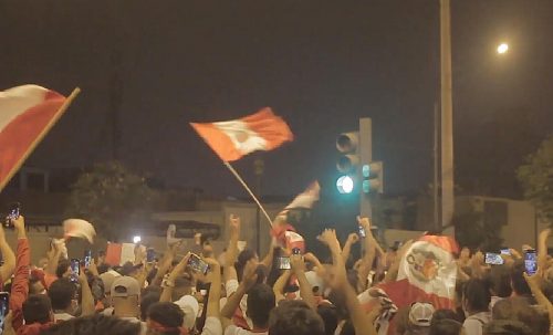 Flags wave and arms gesture during a nighttime protest in Lima on April 5, 2022.