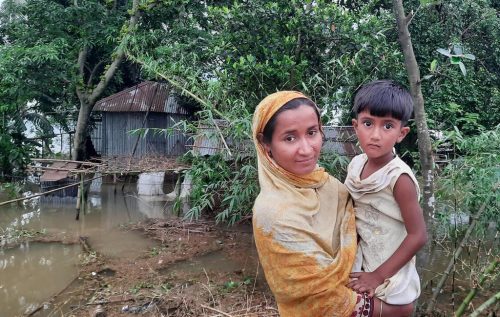 Rukhsana Akhtar Kajol, 28, stands with her daughter Nusrat, 4, outside their tin house that has been inundated and battered in the flood in Jaintapur, Sylhet on 16 May 2022. Their home has been flooded since 9 May.