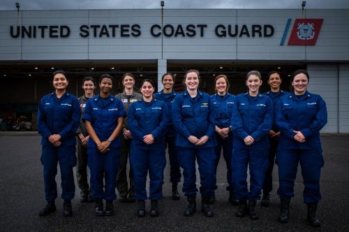 Eleven uniformed female members of the Coast Guard stand in front of building labeled United States Coast Guard. Women of USCG Air Station Savannah.