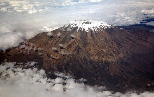 The glacier-covered peak of Mount Kilimanjaro surrounded by clouds, captured out the window of a flight from Dar es Salaam.